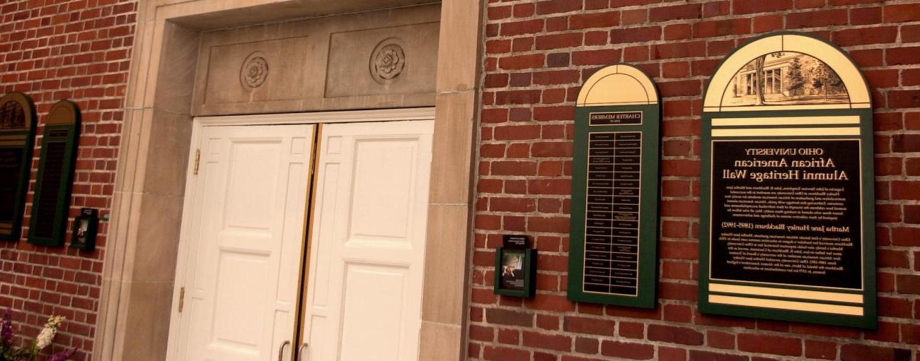 Brick wall with white doors and plaque to left with names.